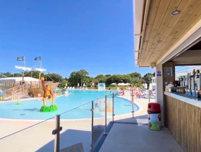 Palm Bay Beach Bar overlooking the outdoor swimming pool at Monkey Tree Holiday Park, with sunny skies and poolside seating.